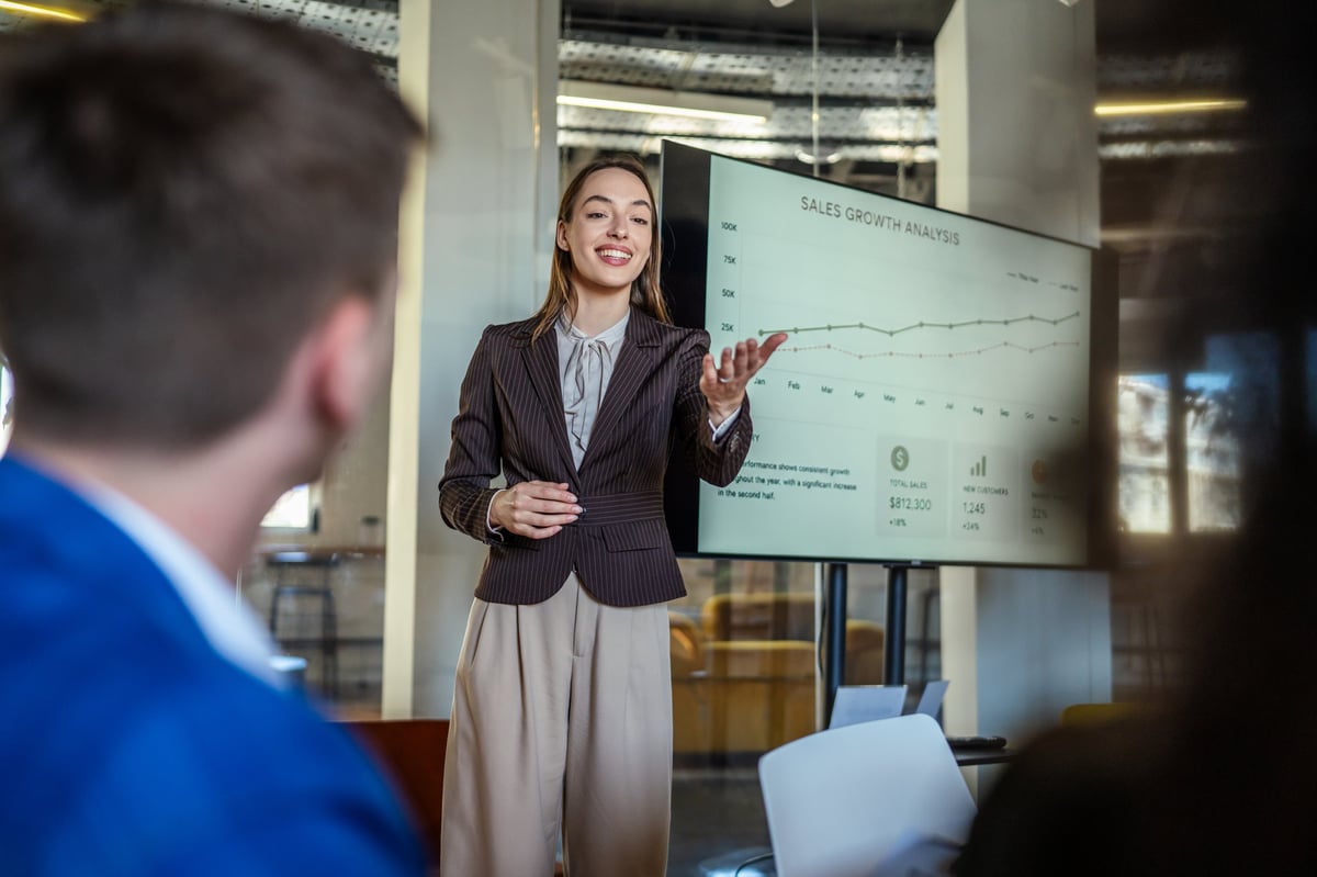 Junior advisor presenting sales growth analysis to a team in a modern office